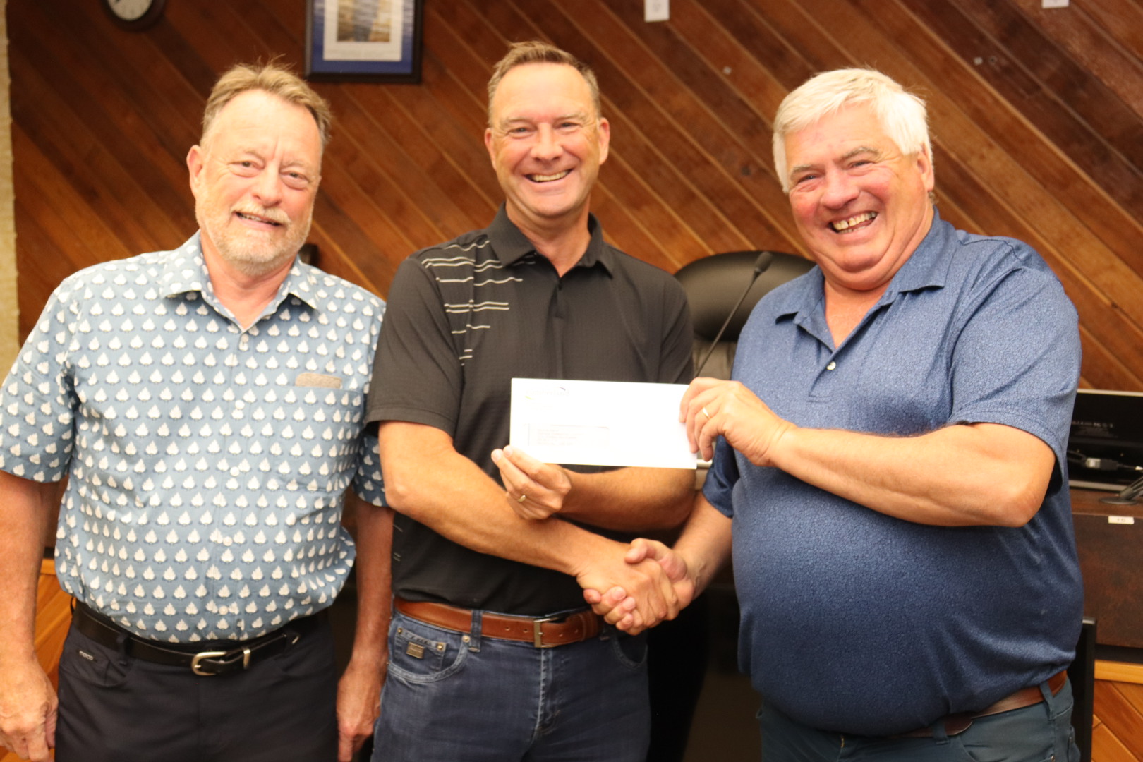 Three men said next to each other holding an envelope with a cheque in it.